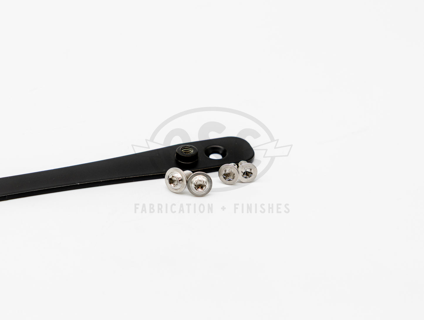 JDM to US license plate adapter made from 6061-T6 aluminum with matte black powder coat, showing countersunk mounting holes and press-fit threaded inserts