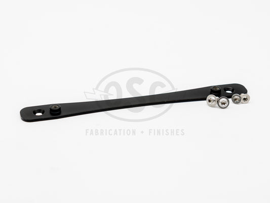 JDM to US license plate adapter made from 6061-T6 aluminum with matte black powder coat, showing countersunk mounting holes and press-fit threaded inserts